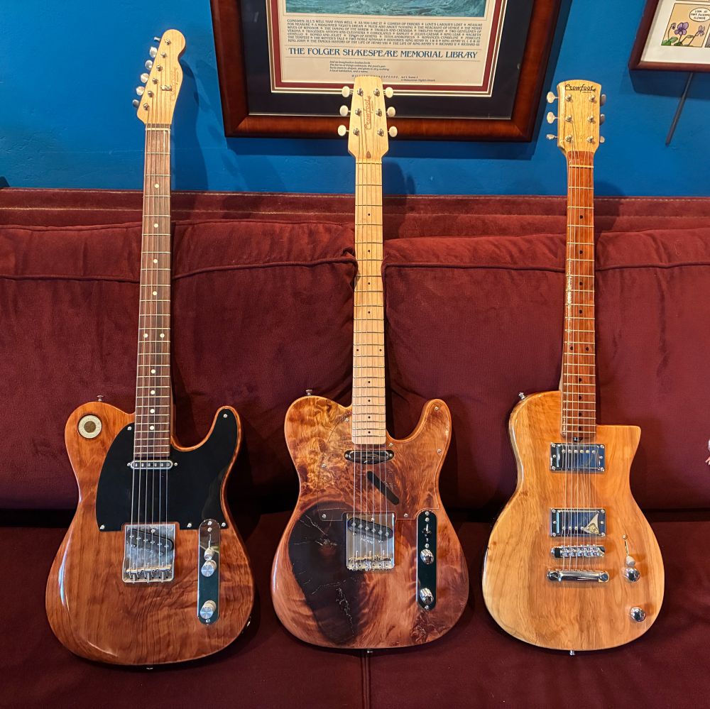 Three guitars resting on a red couch. The wood of their bodies is highly figured, wavy grained redwood with clear lacquer finish.