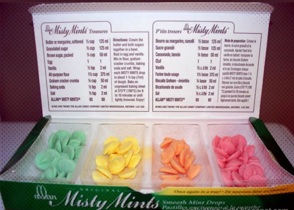 a box of coloured mint discs in light green, yellow, orange, and pink. The mints are in an open box and the container has the mints separated by colour.