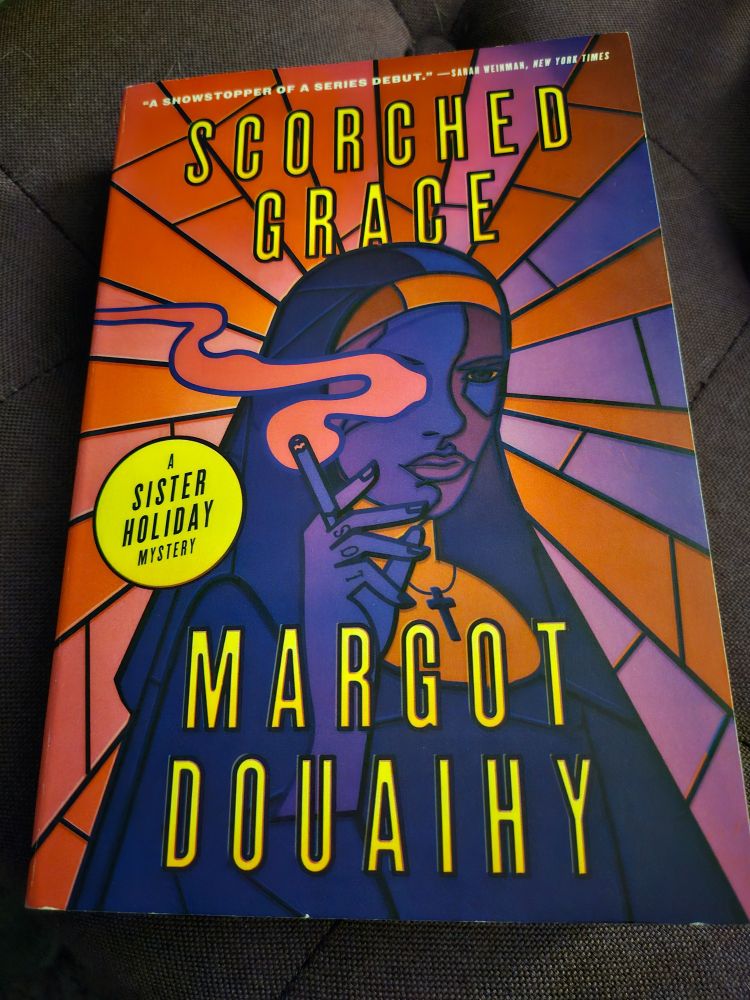 Picture of the book Scorched Grace by Margot Douaihy; Cover features a nun with a cigarette.