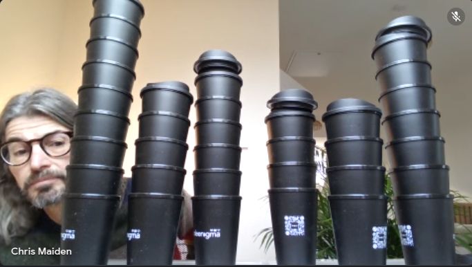 Code Enigma senior developer, Chris Maiden, snapped in a Google Meet behind several stacks of Code Enigma branded re-usable coffee cups, ready to be taken to DrupalCamp England.