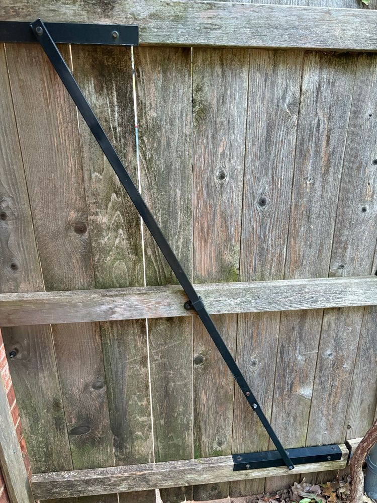 The back side of a cedar fence gate with an angled black brace from one corner to another, diagonally. 