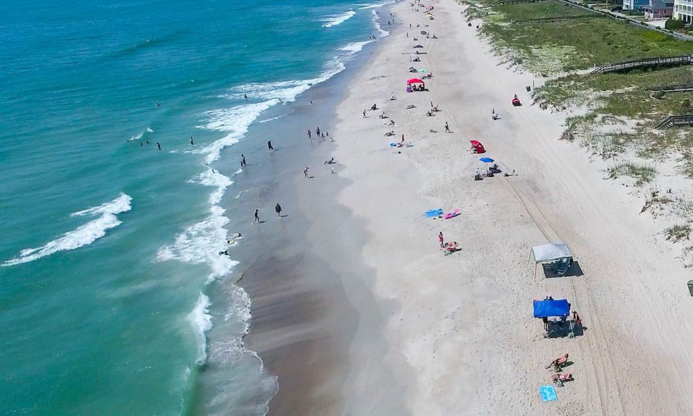 Image of a sunny North Carolina shore, umbrellas and people scattered through the white sand beach.