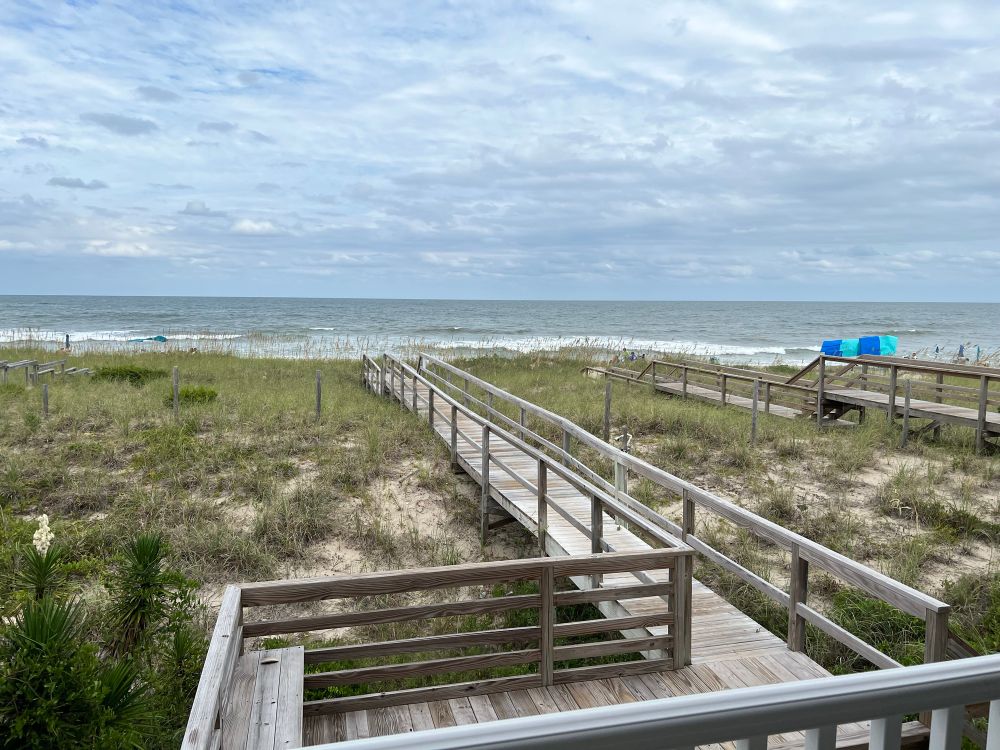 A personal boardwalk to a North Carolina beach. The sky is overcast and the surf is fairly heavy. 