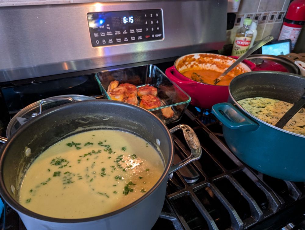 three pots of soup (tomato basil, potato leek, and zuppa toscana) on a stovetop