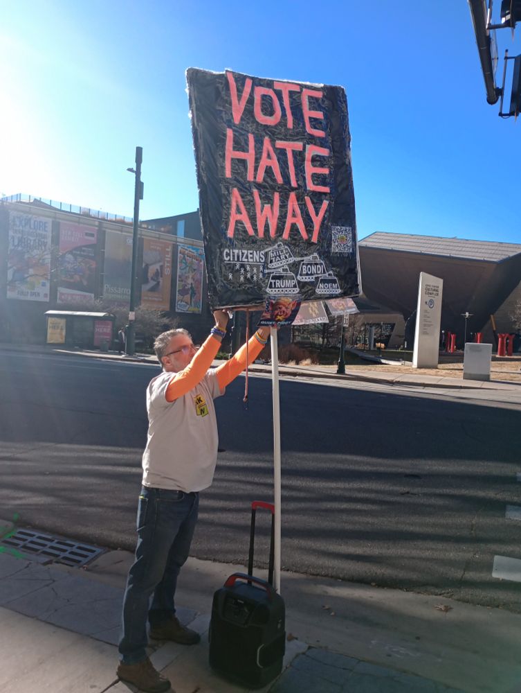 A man holds a large sign reading VOTE HATE AWAY 
