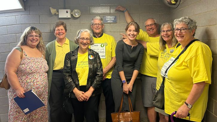 A group of people wearing yellow shirts stand in front of a sign that reads "Tornado Shelter Area".