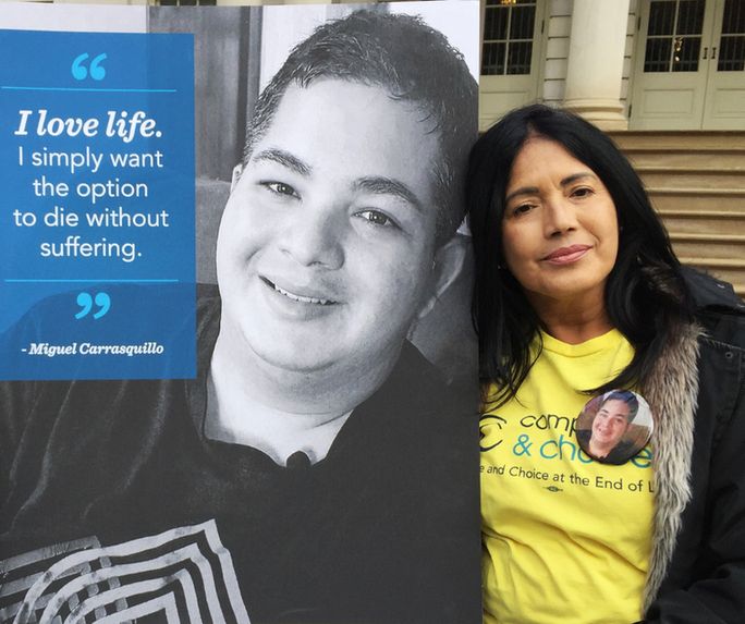 Nilsa stands in front of a poster of Miguel with the quote "I love life. I simply want the option to die without suffering."