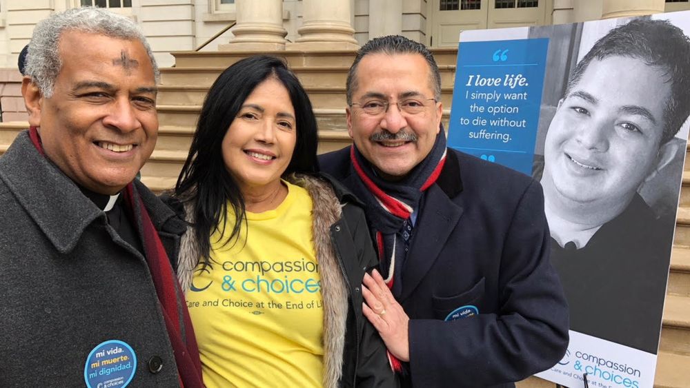 A group photo in front of a poster of Miguel with the quote "I love life. I simply want the option to die without suffering."
