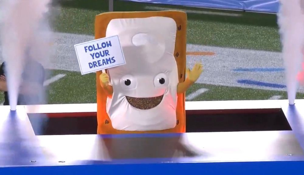 An anthropomorphic pop-tart with a sign that says “follow your dreams” being lowered into a massive toaster 
