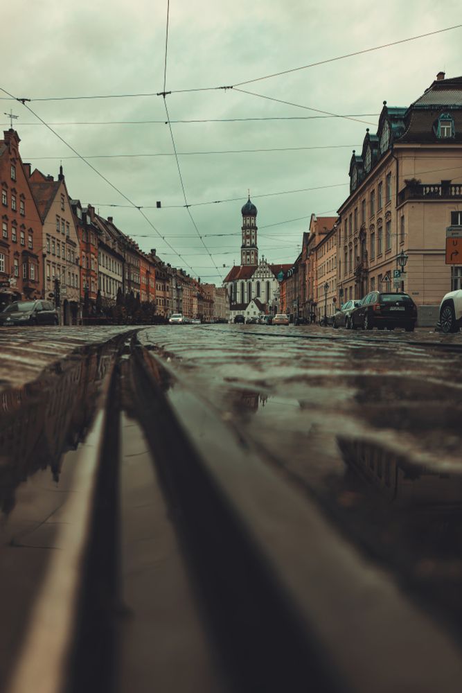 Foto einer Innenstadtstrasse mit Kopfsteinpflaster und Schienen. Pfützen, im Hintergrund eine Kirche