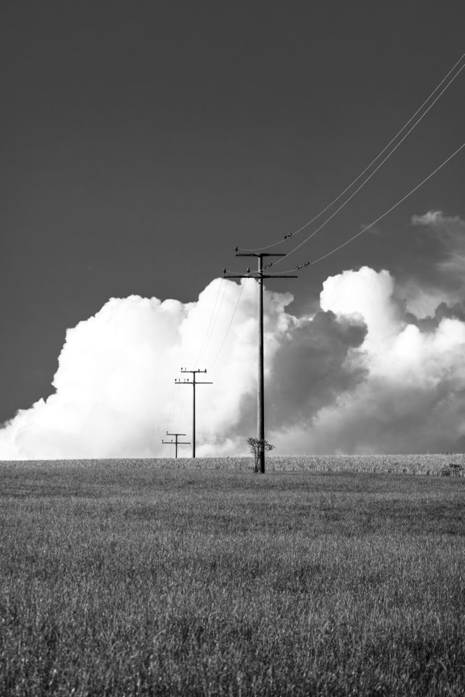 Foto eines Hügels vor einer großen Wolke, darauf Strommasten