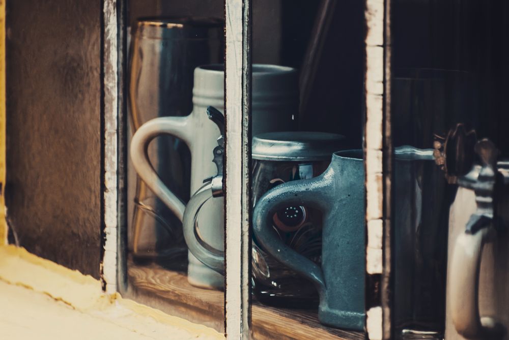 Durch ein altes Fenster hindurch fotografierte Bierkrugsammlung