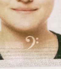 ausschnitt vom scan eines reisepasses, genauer: ein ausschnitt des passbildes bei dem auf höhe des kehlkopfes ein bassschlüssel als wasserzeichen angebracht ist.