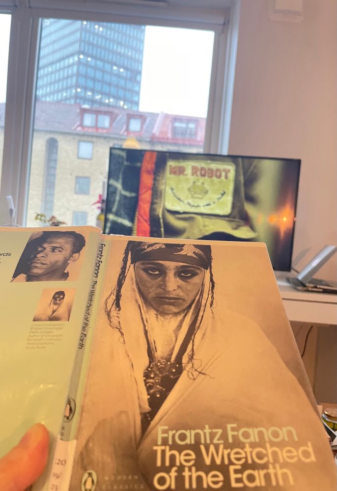 a copy of frantz fanon's the wretched of the earth in the foreground, a tv-screen playing mr. robot in the background