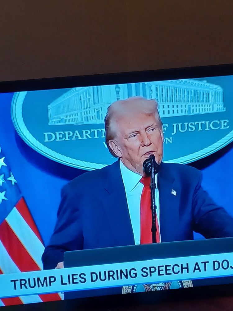 Words behind his head say "depart justice" as caption says "Lies during speech at DOJ". 