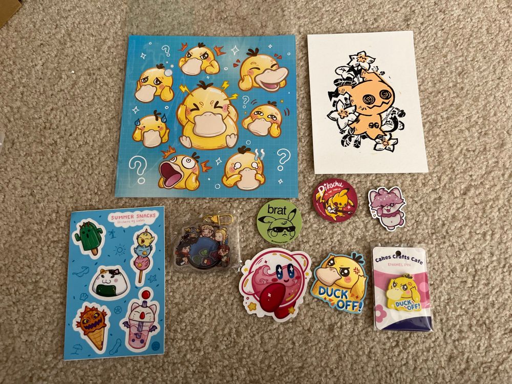 Merch from Cakes Crafts, consisting of: a square print of Psyduck’s various moods; yellow and black ink print of Mimikyu with flowers; sticker sheet of cute FFXIV characters; Delicious In Dungeon shaker charm; crystal Kirby sticker; Pikachu “brat” sticker; “Pikachu vs. the world” sticker; Psyduck “duck off!”sticker; same Psyduck but as an enamel pin; Cakes’ mascot sticker.