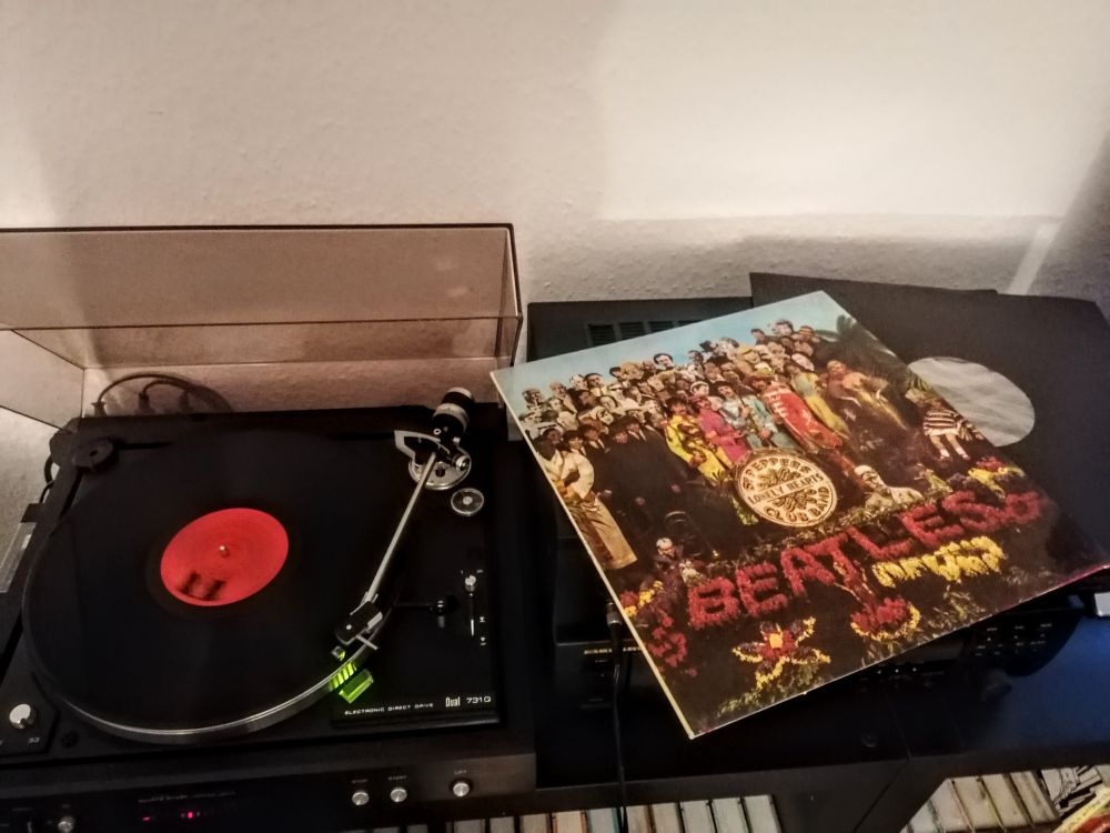 Cover to Sergeant Pepper's Lonely Hearts Club Band LP by The Beatles, depicted is a bunch of popular people surrounding the band that's standing in front of a floral arrangement of their band name 