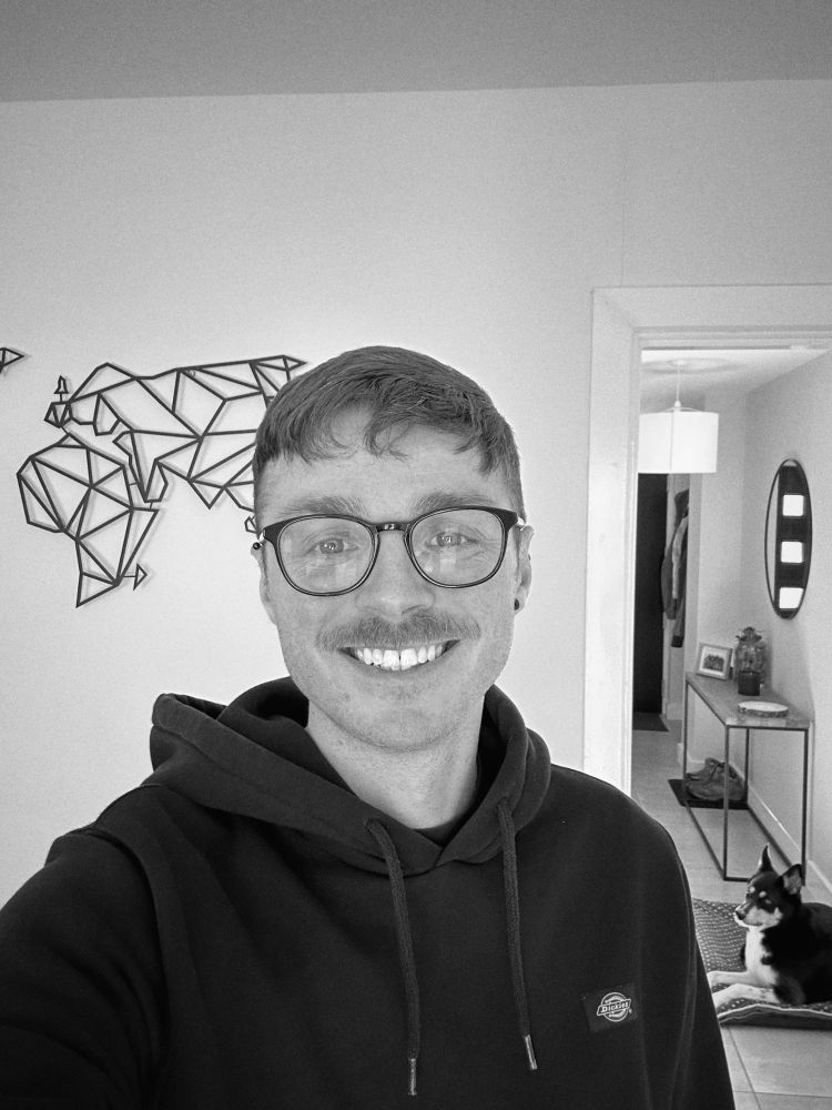 Monochrome selfie of me smiling (but tired) with Skye, the dog, in the background - clearly stealing the spotlight. Unclear who this post is really about.