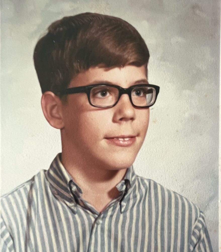 Grade school portrait: brown hair, vertical striped shirt, new glasses. My nerd cred photo.