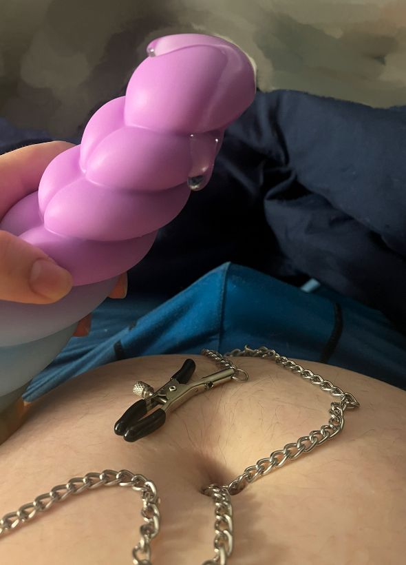 A purple dildo with several ridges and lube dripping from the tip, one if the nipple clamps lay on my stomach and there is a bulge in my boxers