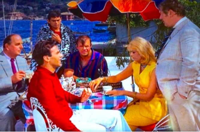 A colorful photo of the cast of the heist film Topkapi enjoying tea along the water while plotting their caper. 