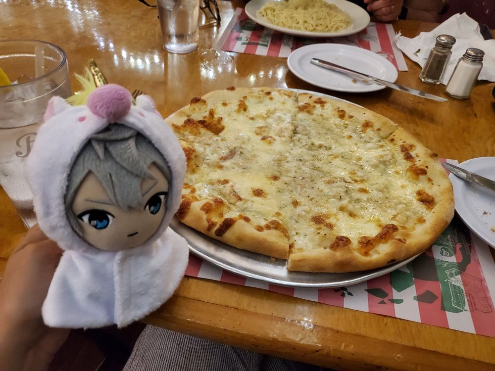 izumi sena plushie in a unicorn outfit posed in front of shrimp pizza