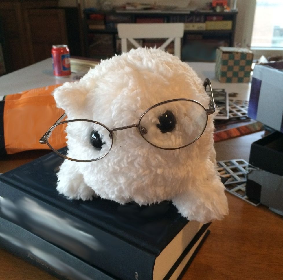 Baba standing on a book wearing metal glasses, with a bunch of clutter behind them