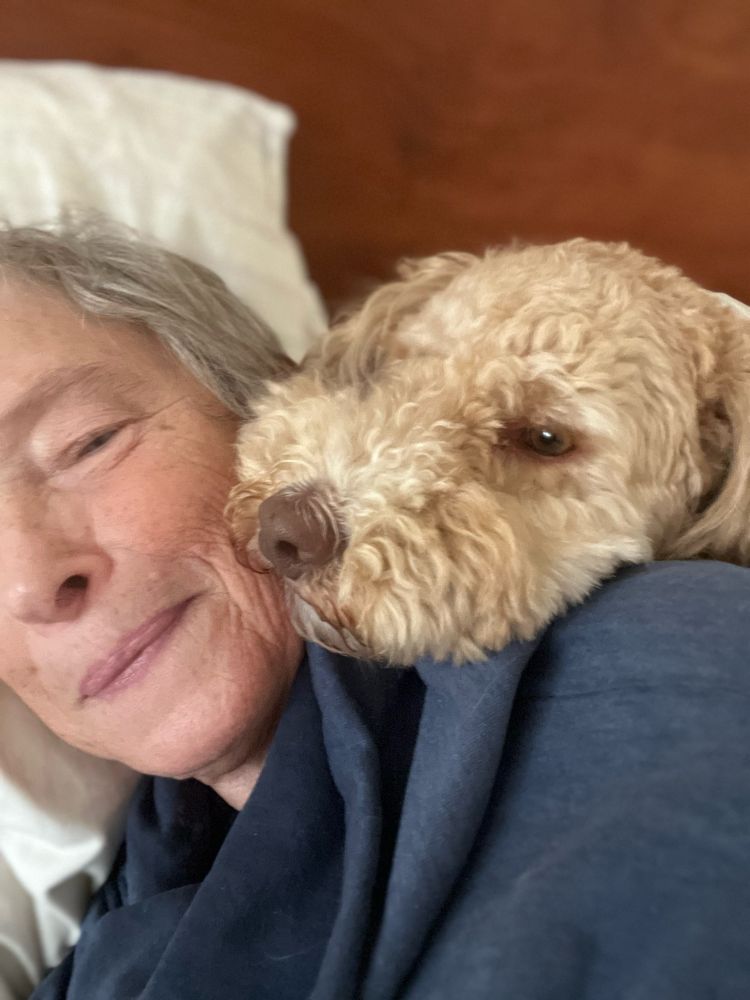 Half of a woman’s face. A fuzzy tan dog has his head on her shoulder.
