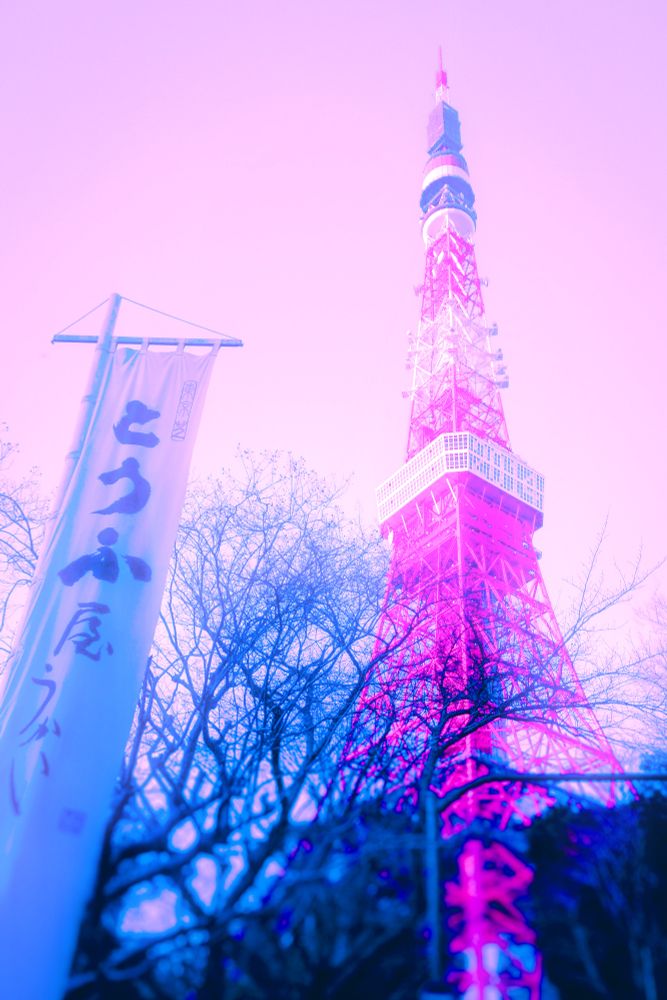 Image of Tokyo Tower from a low angle, looking up with trees in front. With a vertical flag/banner on the lower left side