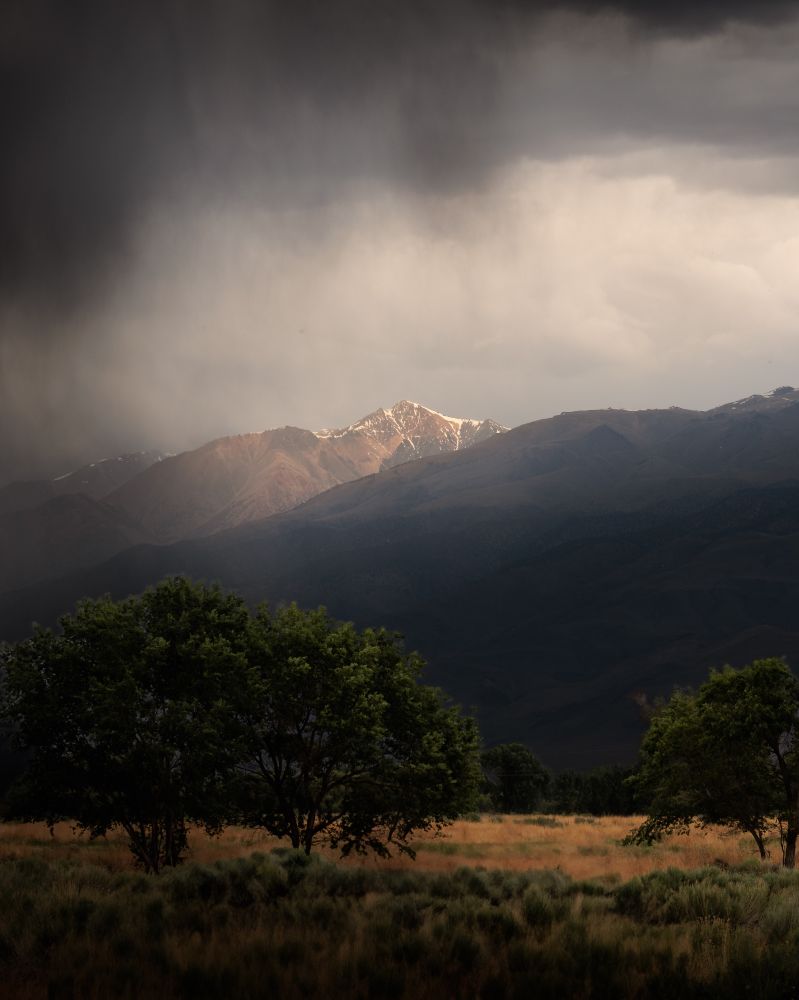 The mountains shrouded in clouds and rain, with the sun coming through to spotlight the mountain.