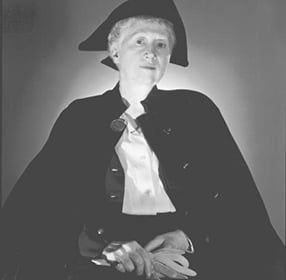 Photo of the poet Marianne Moore pictured in her later years in a tri-corn hat and cape.
