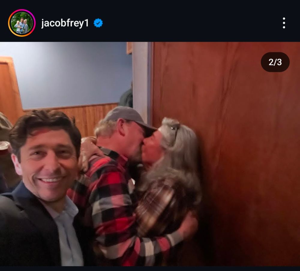 Mayor Jacob Frey taking a selfie in front of two gay men in flannels kissing
