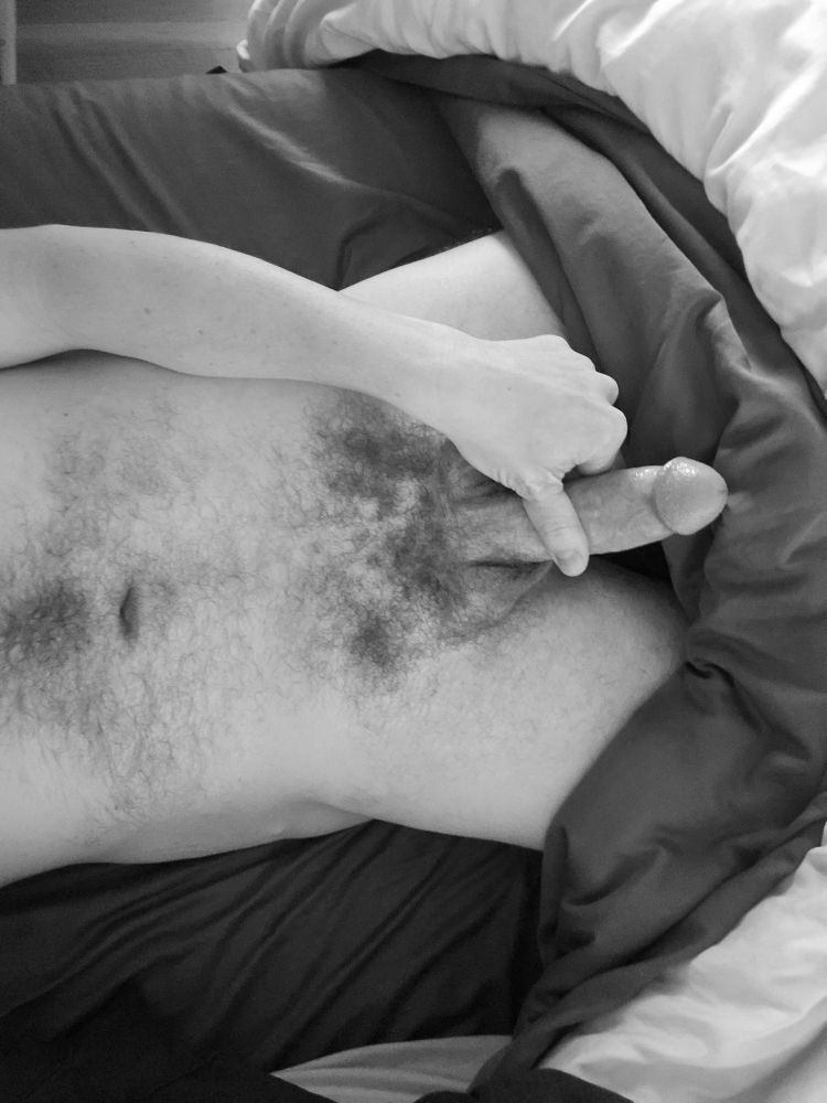 Black and white selfie of Loadz' torso while he points his cock away from the camera in bed.