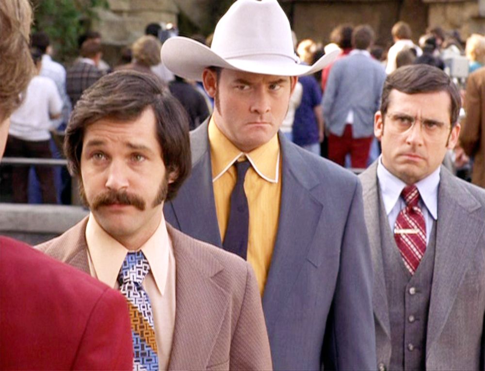 Three men in 70s business attire stand staring at another man offscreen. They are Paul Rudd, David Koechner, and Steve Carrell from Anchorman. 