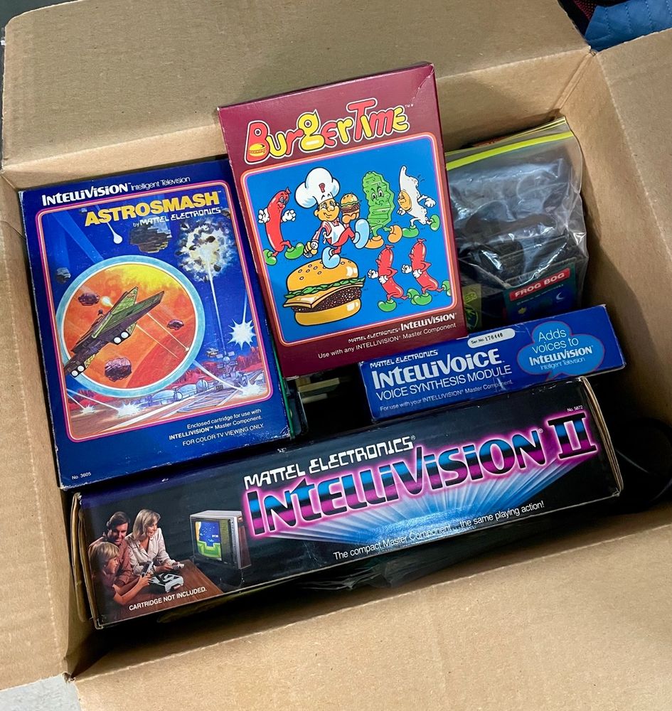 Box containing and Intellivision II game console, IntelliVoice module, and several cartridges including boxed copies of Astrosmash and BurgerTime.