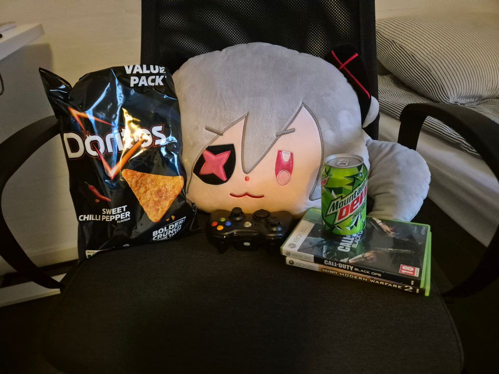 A photo of an El Fail Cushion sitting on an IKEA Markus office chair next to a bag of Doritos and A Can of Mountain Dew, there's also an Xbox 360 Controller and two Call of Duty games