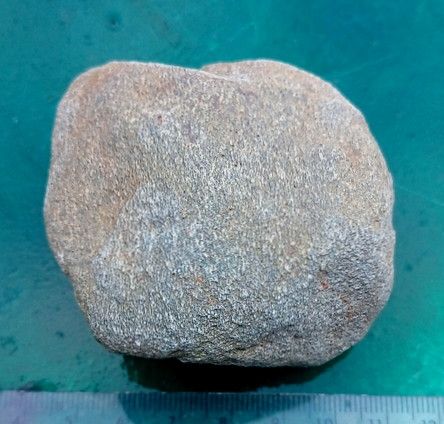 A glacial erratic pebble - this could be classified as a sillimanite gneiss. It is greenish-grey in colour, with white and blue-green crystals with co-aligned fabric orientation.