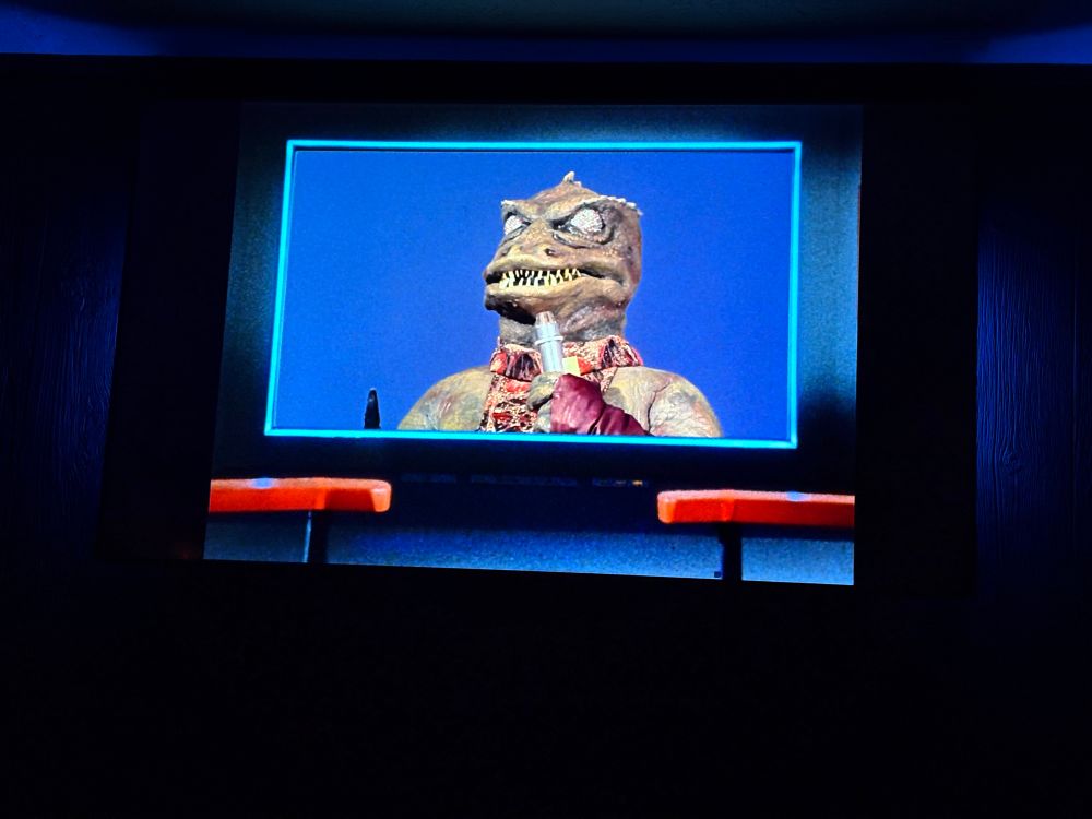 A television playing an episode of Star Trek showing a man in a green reptilian suit with glowing eyes as the Gorn commander.
