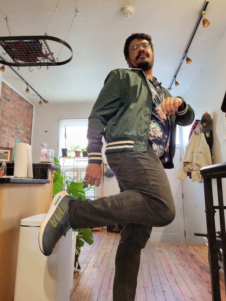 Me doing an outfit check consisting of a green jacket, green shoes, black jeans, and a blue floral shirt