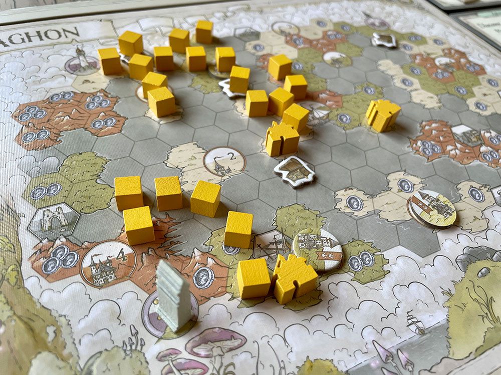 An example board from Guild of Merchant Explorers, with trails of exploration cubes, villages, and other pieces places over a hex-map of a fantasy world.