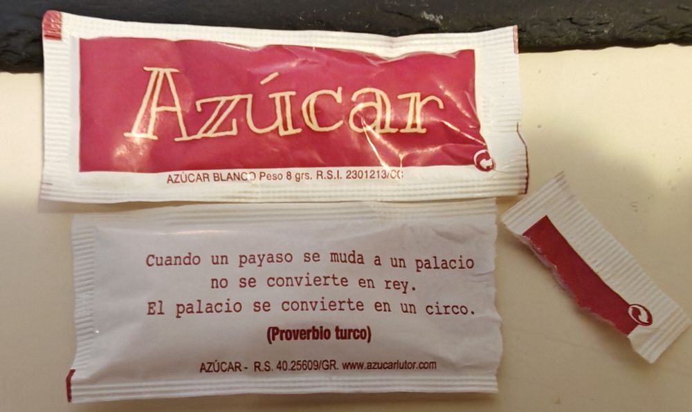 Primer plano de un sobre de azúcar en el que se puede leer "Cuando un payaso se muda a un palacio no se convierte en rey. El palacio se convierte en un circo. (Proverbio turco)"