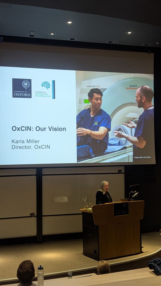 A woman standing at a podium presenting a PowerPoint presentation slide stating "OxCIN: our vision"