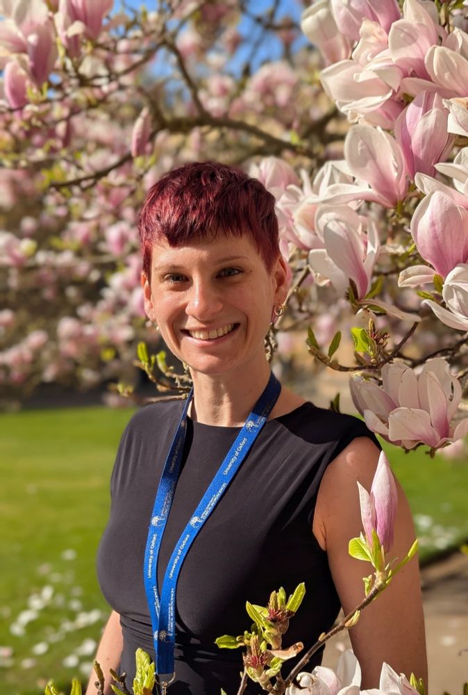 A picture of a woman with short red hair smiling in front of a pink magnolia tree.