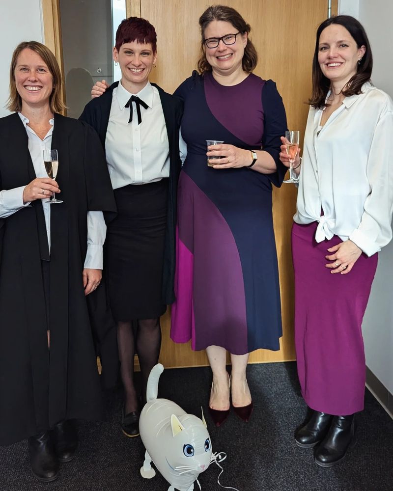 A group of four women in academic dress, smiling whilst holding glasses of Champagne.