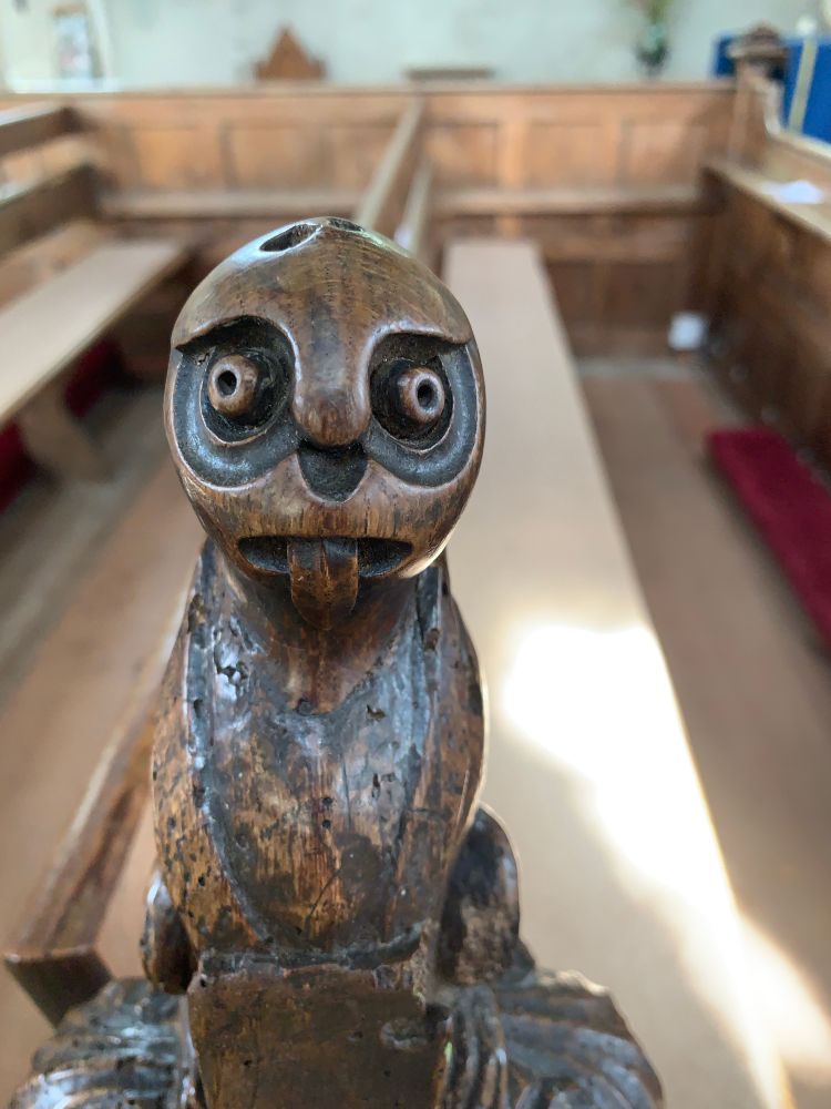 Carved figure with bulgy eyes & protruding tongue on a pew in St Margaret’s church, Cley