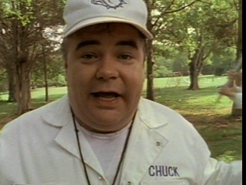 Gailard Sartain as 'Chuck' from one of the Ernest films. He is wearing a white hat and white jacket with the name 'Chuck' in the breast. He is soaking directly to the camera. 