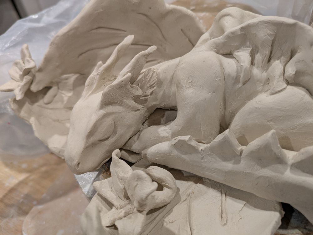 A white porcelain baby sleeping dragon on a nest of leaves with flowers scattered around