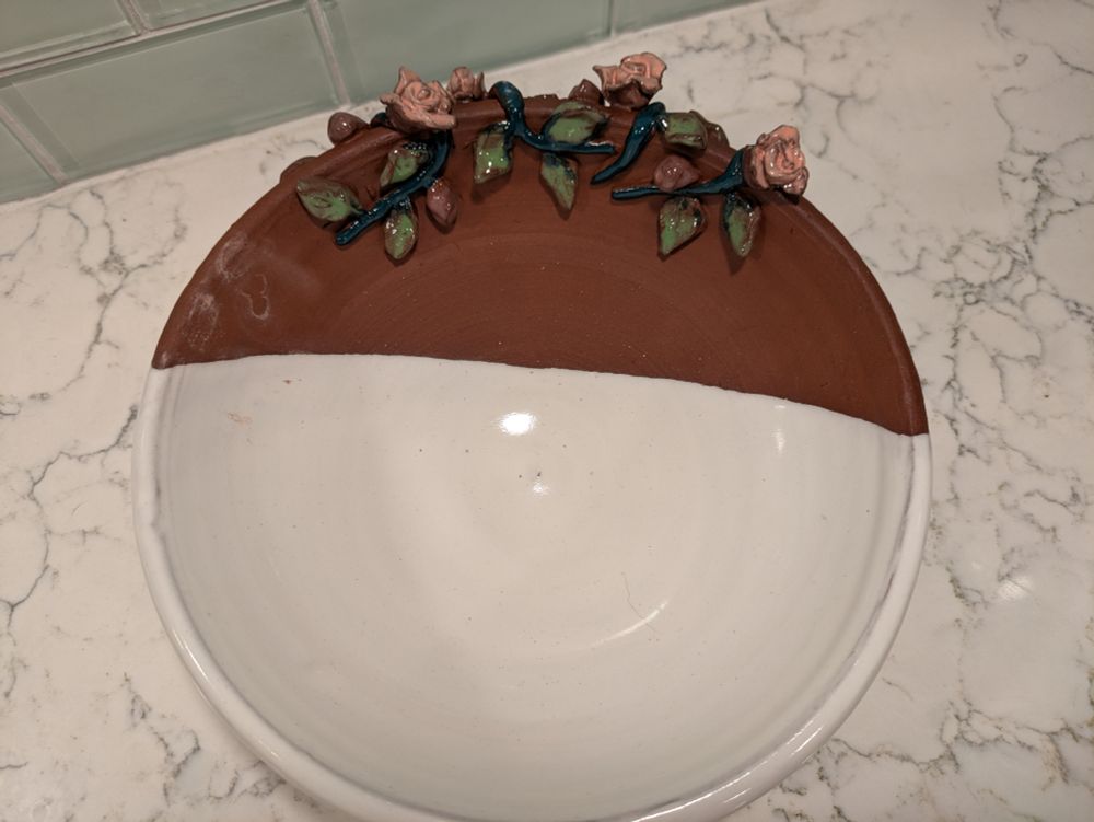 A bowl with white glaze, unglazed earthenware, and tiny sculpted roses around the side