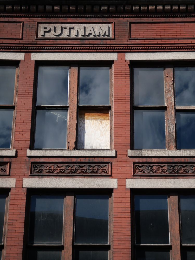 the top few floors of a brick building, with the sky reflected in the windows. PUTNAM is carved into granite.