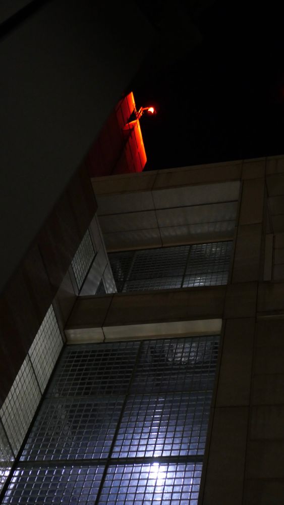 light shining down through glass block windows at night. a red warning light glows from the top of the building.